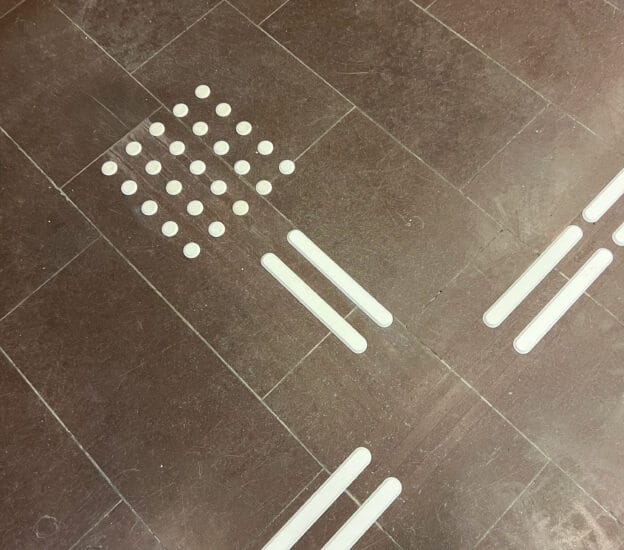 Vita taktila ledstavar med stoppyta på brunt stengolv.