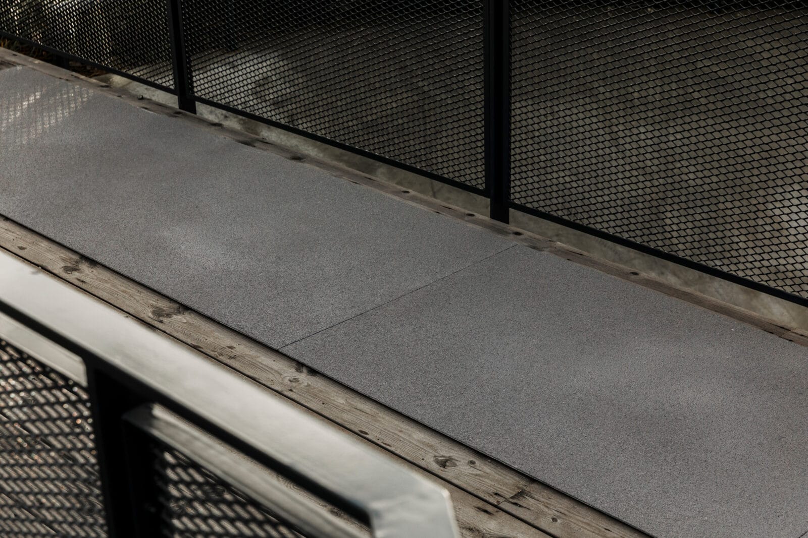 Svart halkskyddsskiva i glasfiber på gångbro i trä med svarta metallräcken